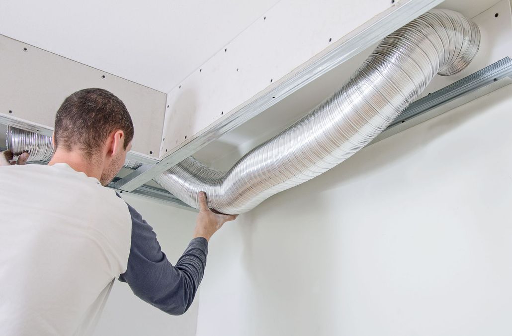Man installing flexible silver ductwork in ceiling.