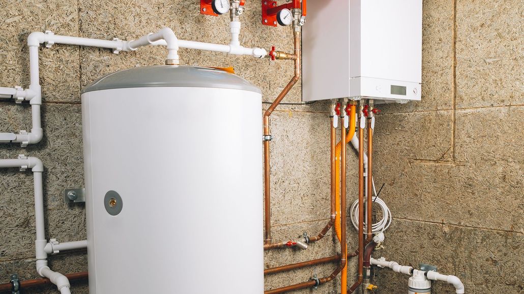 White water heater and boiler with pipes and gauges against a concrete wall.