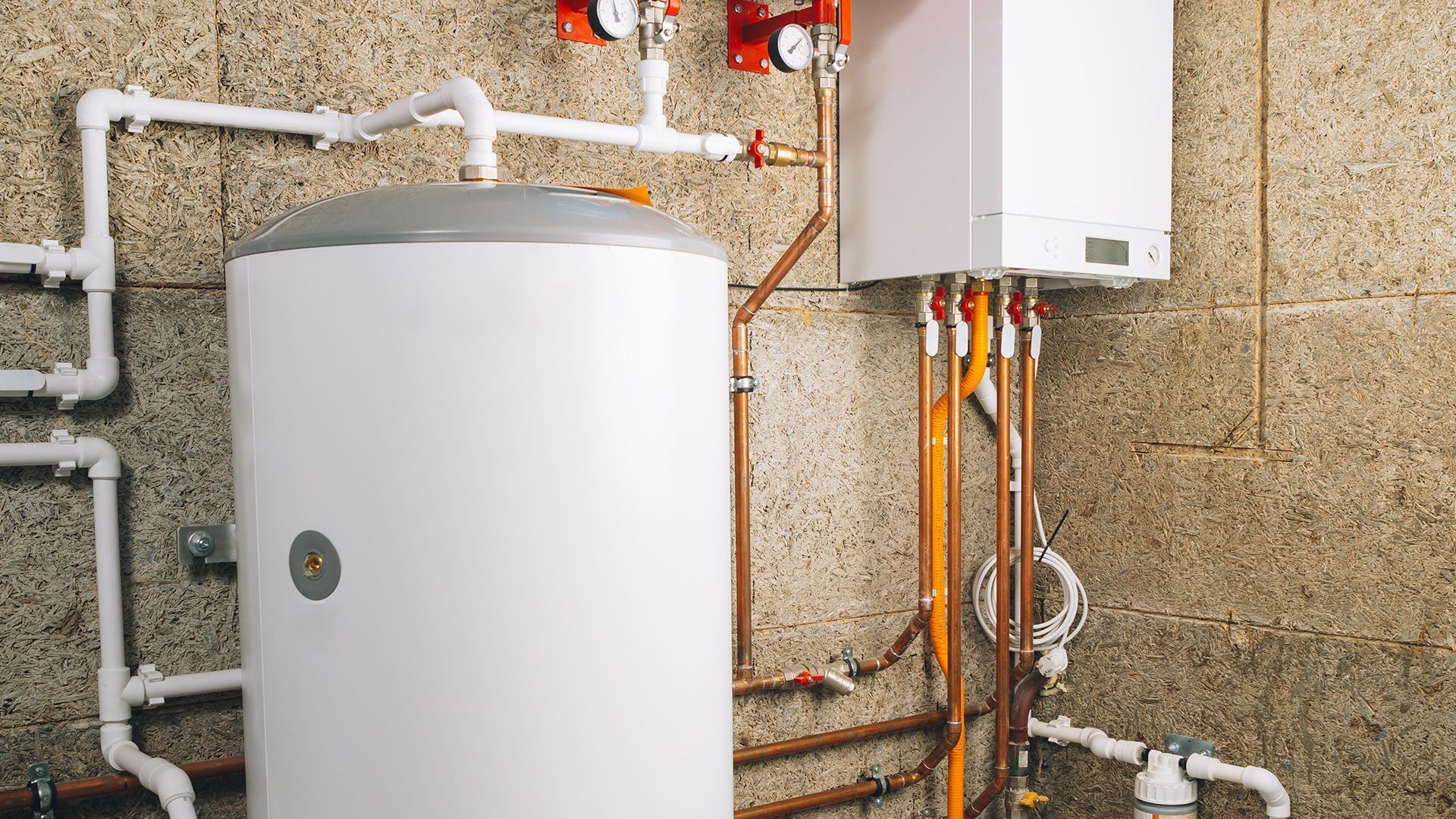 White water heater and boiler with pipes and gauges against a concrete wall.