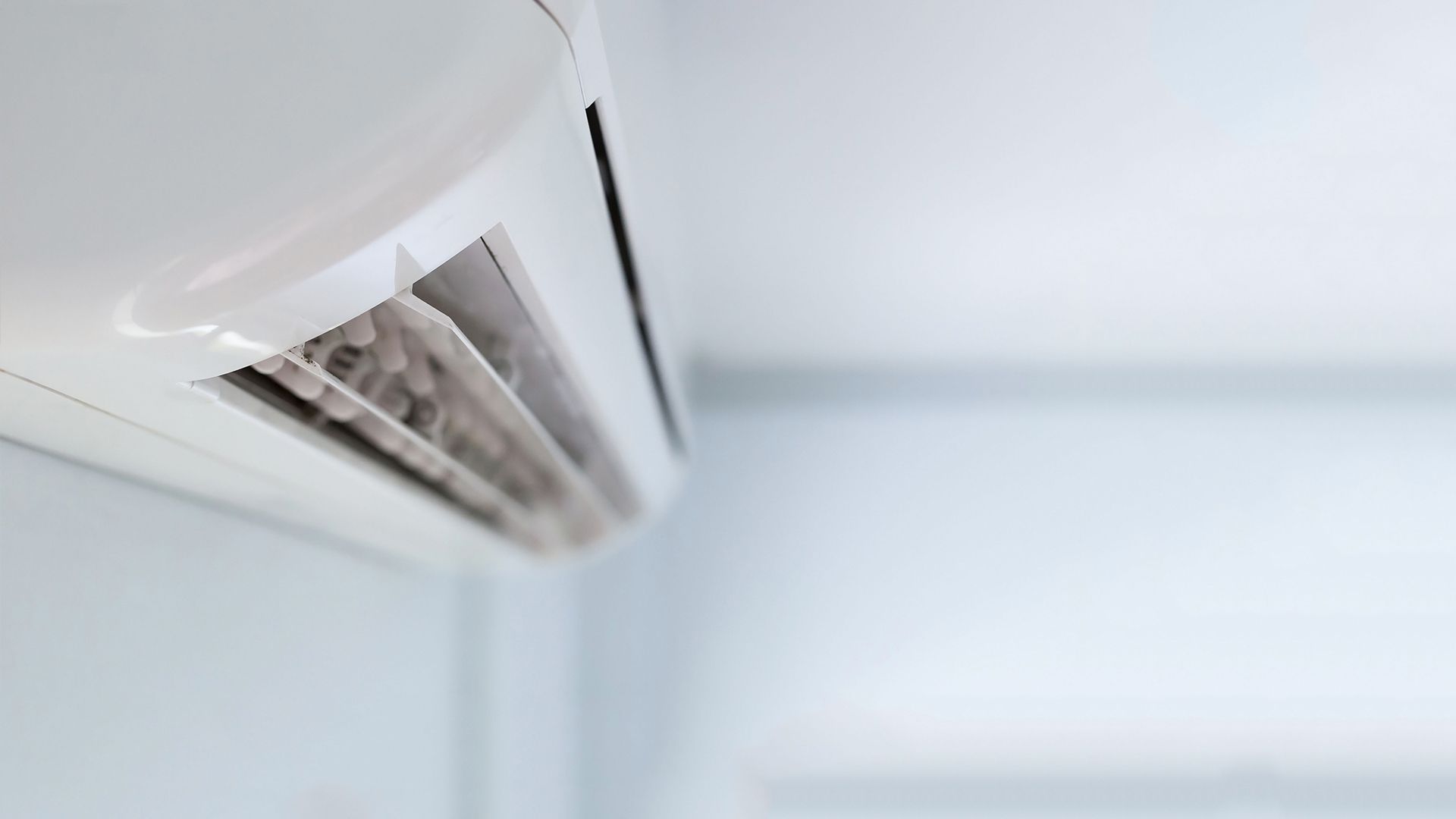 Close-up of a white air conditioner, dirty vent slats, mounted on a white wall.