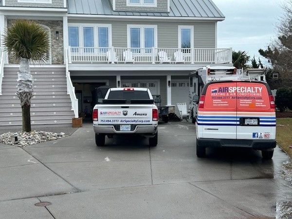 A two-story gray house with a white garage. Two service vehicles are parked in the driveway.