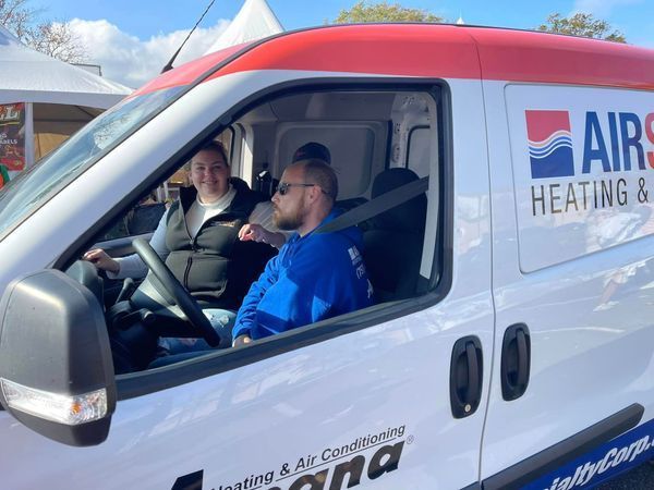 Two people sit in a white Air Spa Heating & Air van. Woman drives, man next to her, both wearing seatbelts.
