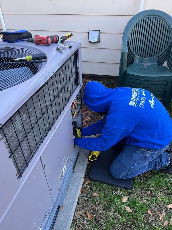 HVAC technician repairs an air conditioning unit outside a home. The person kneels while working.