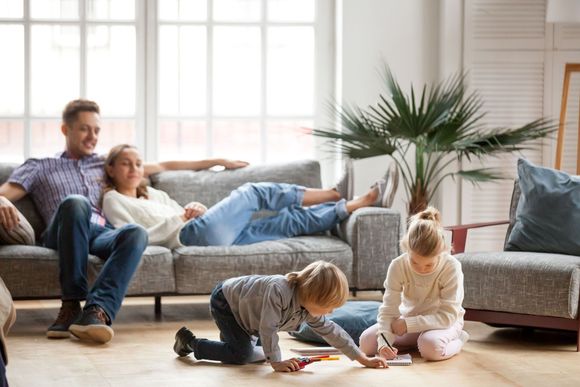 Family relaxing in living room: parents on couch, two children playing on floor.