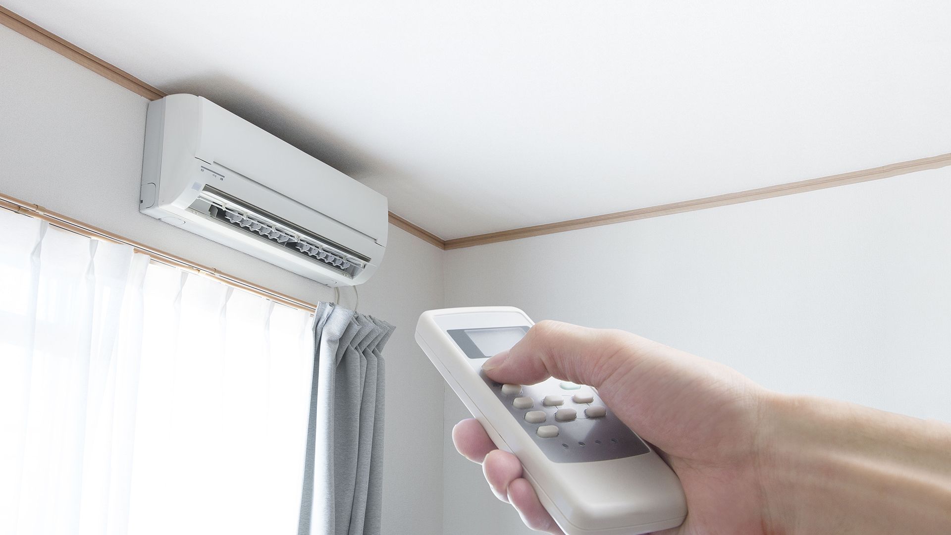 Hand pointing remote control at a white wall-mounted air conditioner.