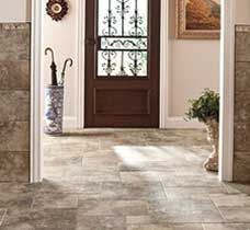 Tiled entryway with brown door, decorative umbrella stand, and artwork. Sunlight through the doorway.