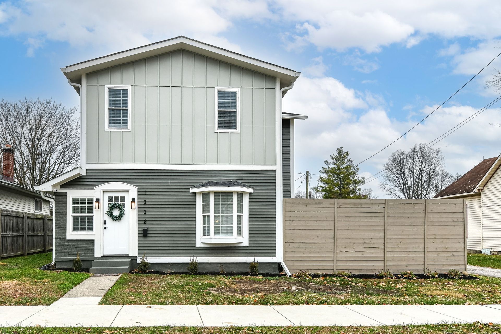 Two-story house with gray siding, white trim, and a small front yard with a wooden fence.
