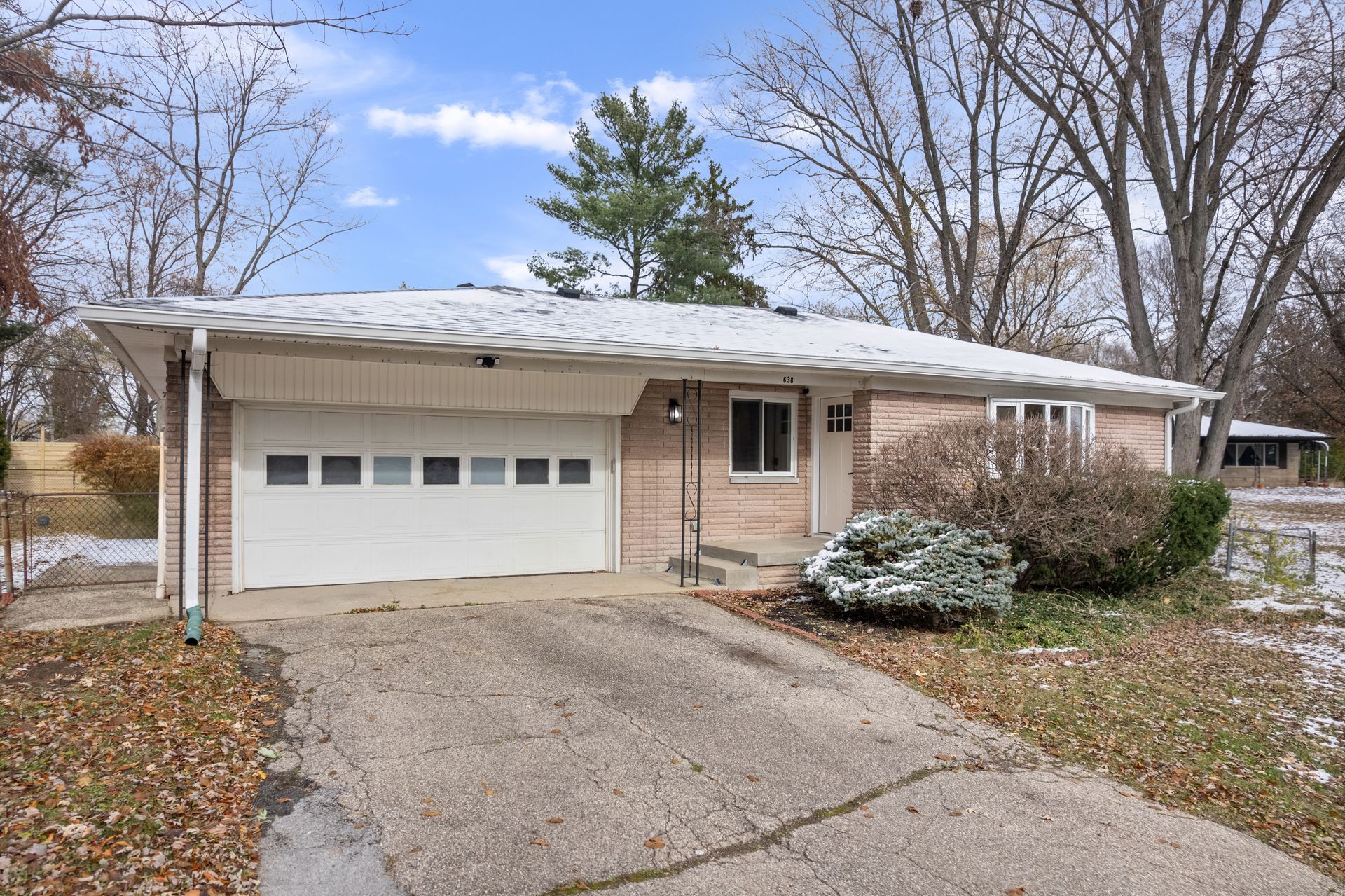 Brick ranch-style house with attached garage, snow on roof and bushes, cloudy sky.