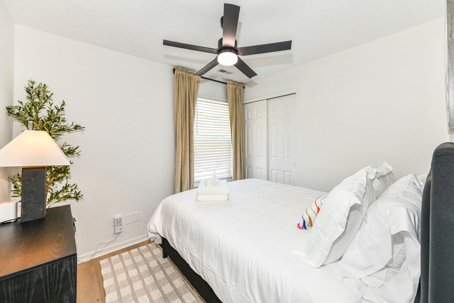 Bedroom with a white bed, beige curtains, and a black ceiling fan.