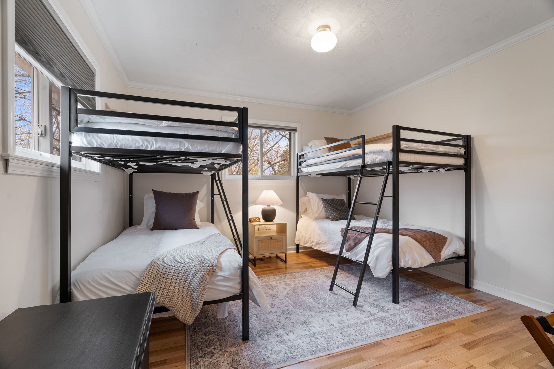 Bedroom with two black metal bunk beds, white bedding, and a neutral rug on wood flooring.
