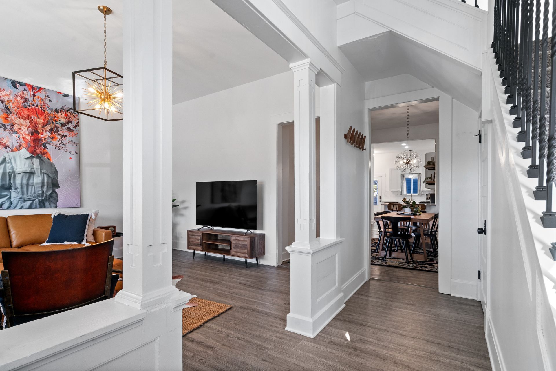 Bright, modern home interior with white columns, hardwood floors, and a view of the living room and staircase.