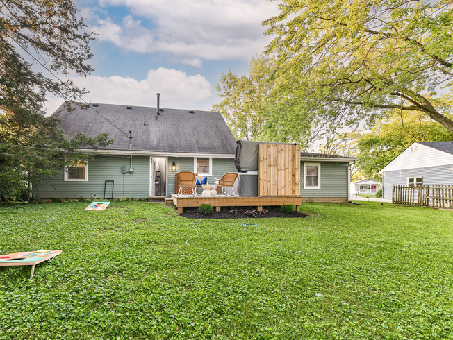 Backyard with a green lawn, wooden deck, small house, and trees under a cloudy sky.