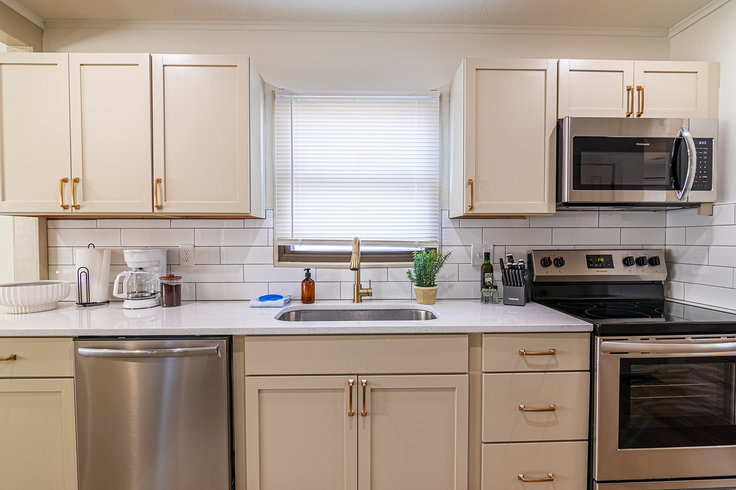 A kitchen with white cabinets, stainless steel appliances, and a window above the sink.