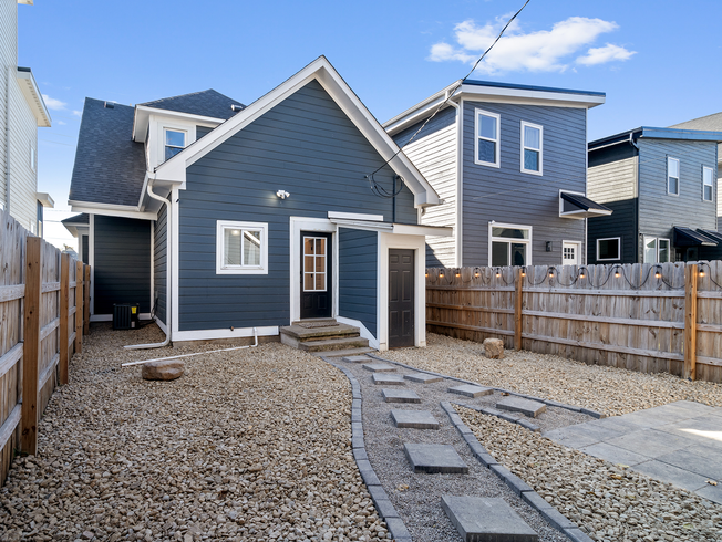Backyard view of a dark blue house with a stone pathway and gravel yard, next to a wooden fence.
