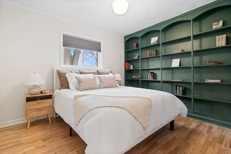 Bedroom with a bed, nightstand, and green built-in bookshelves against a white wall and wood floor.