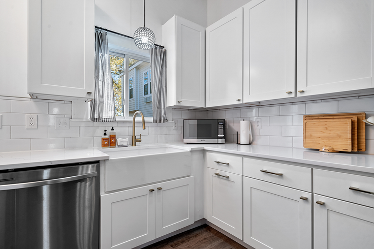 White kitchen with stainless steel appliances, white cabinets, and a farmhouse sink.