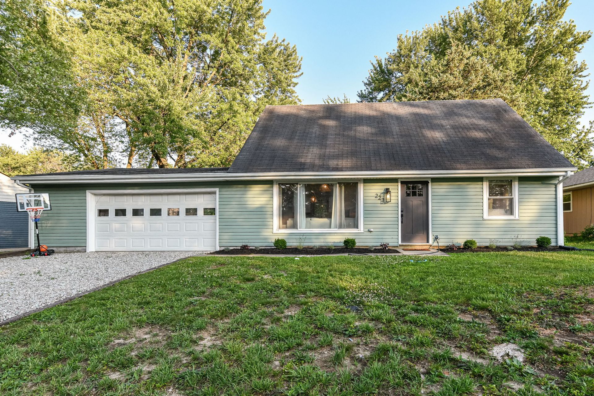 Green house with attached garage, gravel driveway, and a patch of grass.