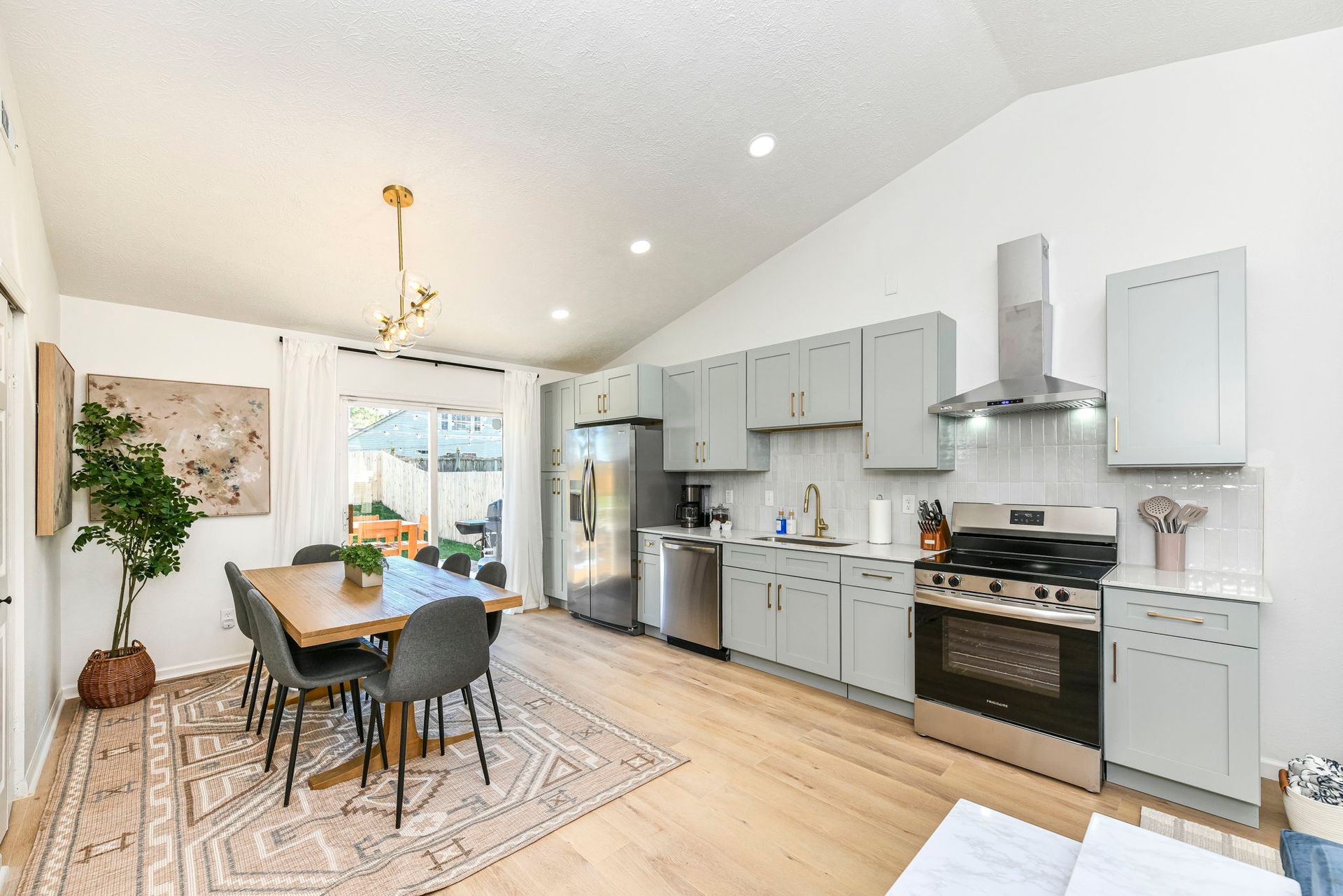 Open kitchen and dining area with light blue cabinets, stainless steel appliances, and wood table.