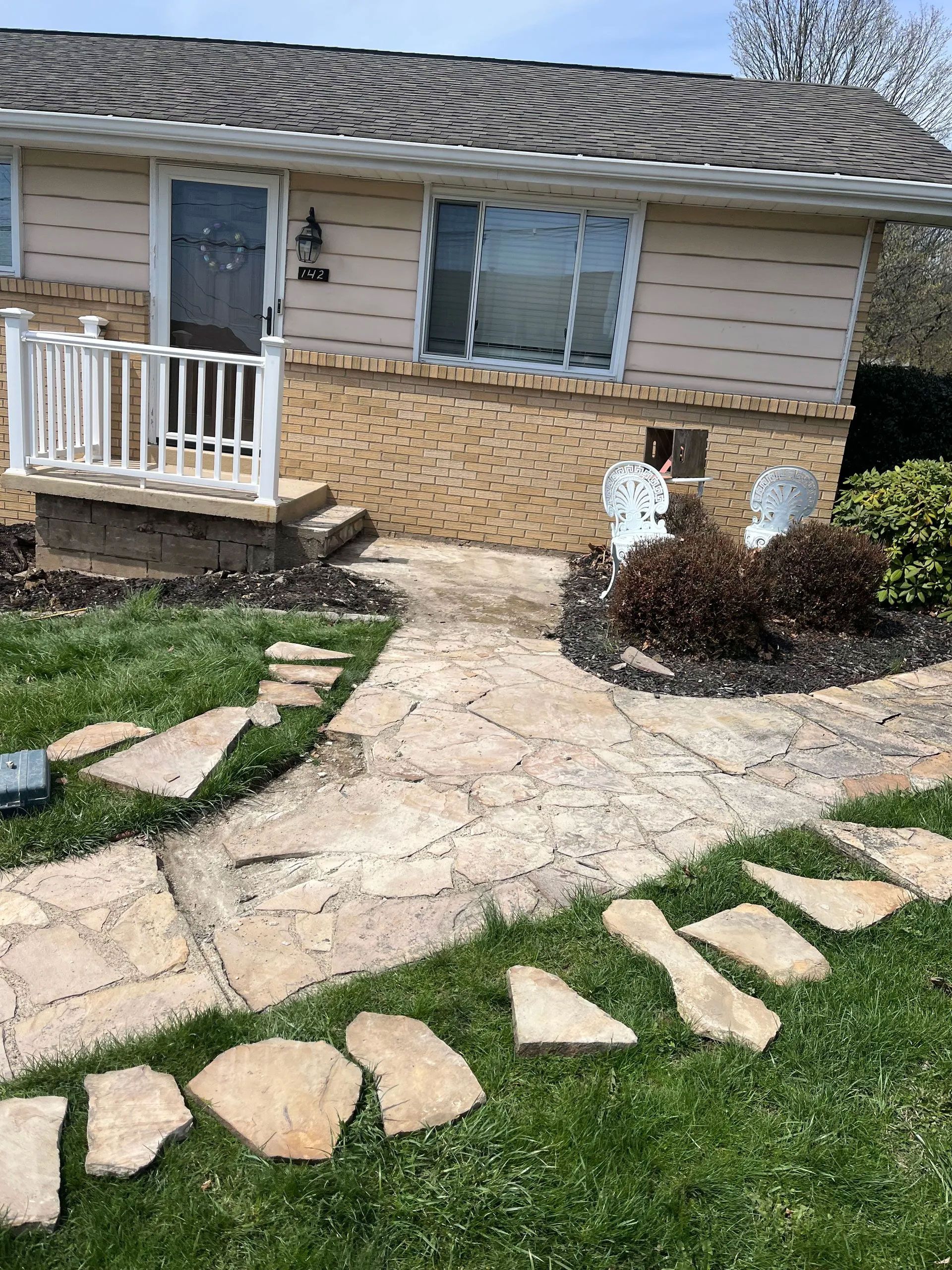 Stone pathway leading to a beige house with a small porch and landscaping.