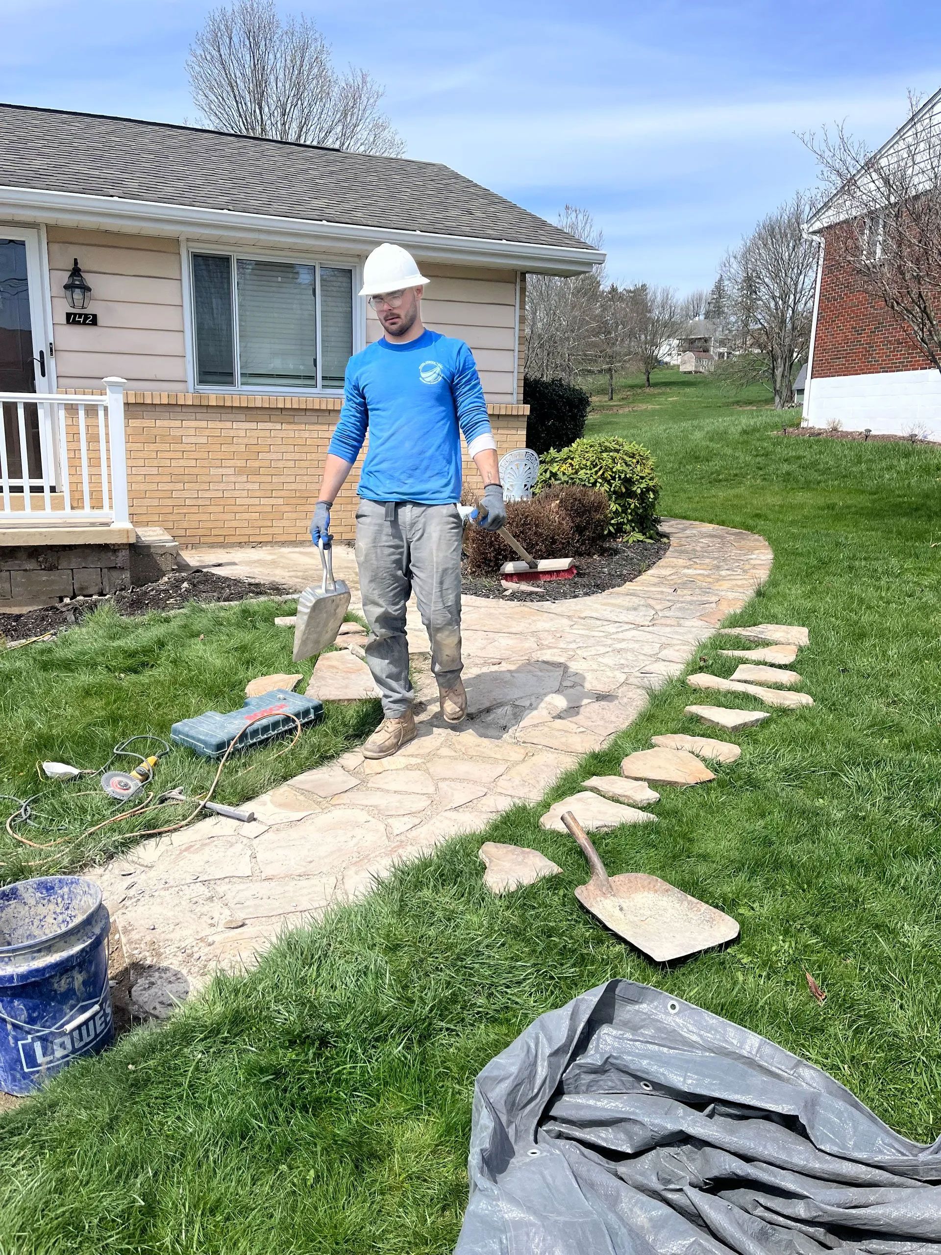 Construction worker laying stone pathway in front of a house on a sunny day.