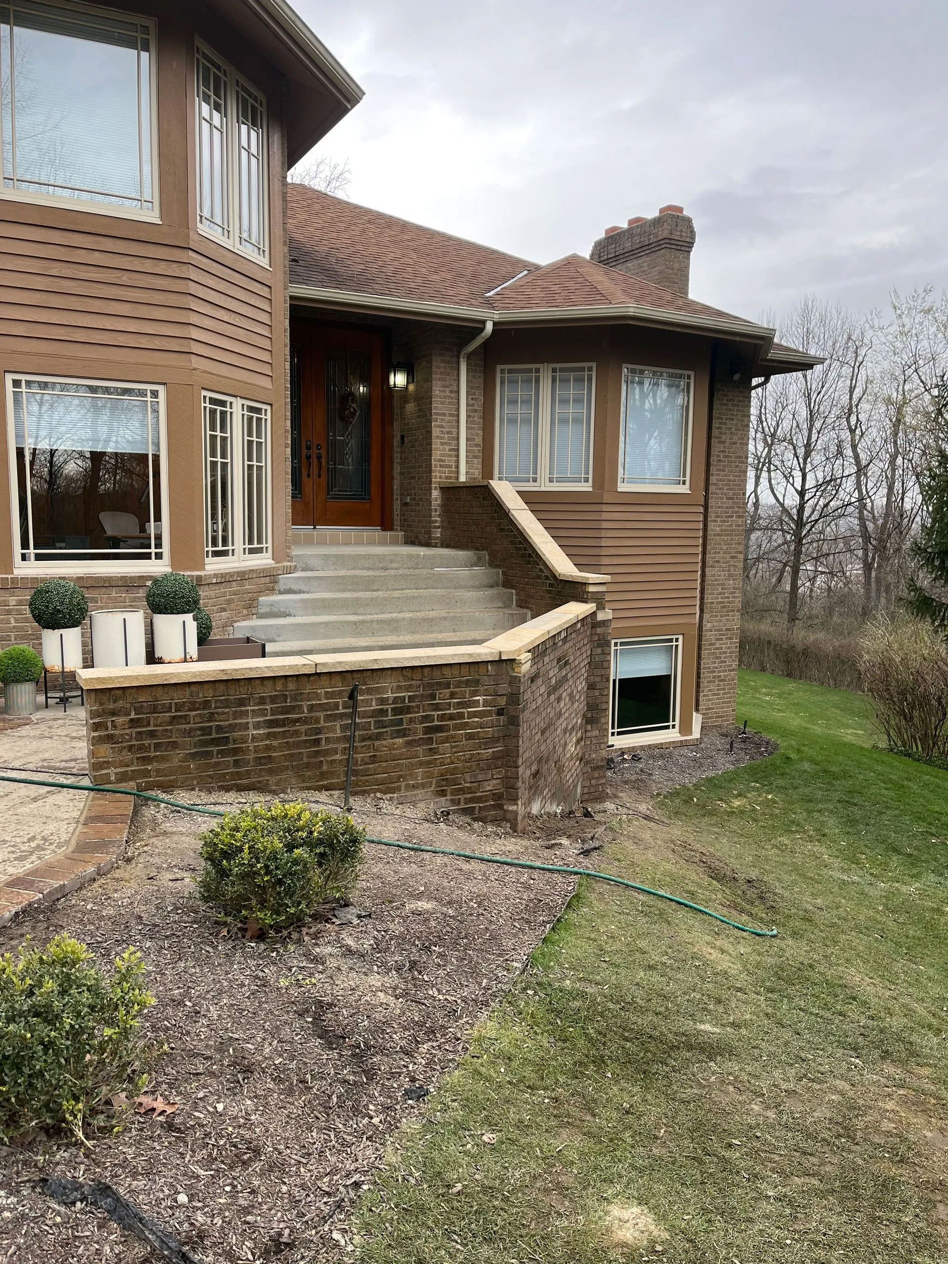 Two-story home with stone facade, steps leading to the front door, and a sloping lawn.