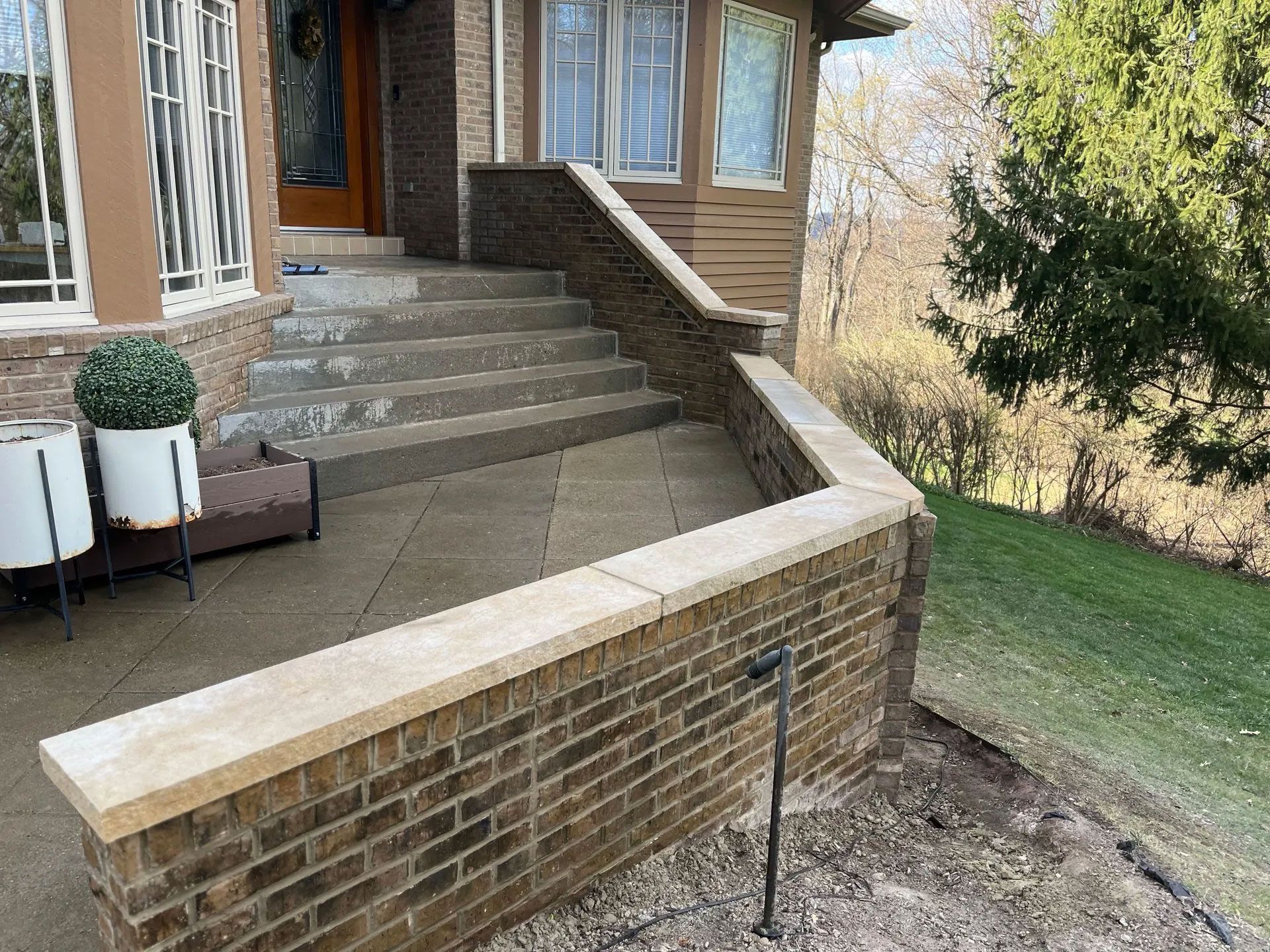 Brick and stone steps lead up to a porch with a brown brick wall and beige stone caps.