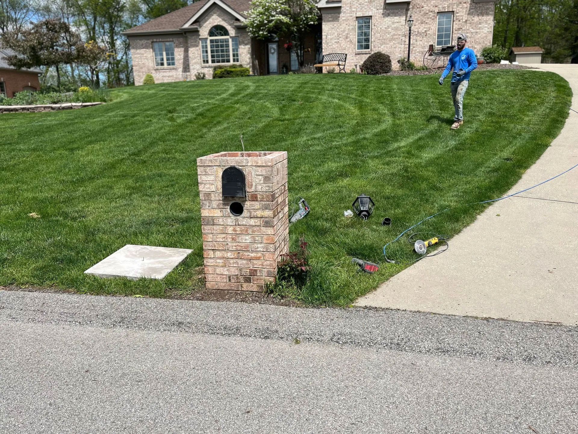 Brick mailbox on a lawn with a person working on the grass. House in the background.