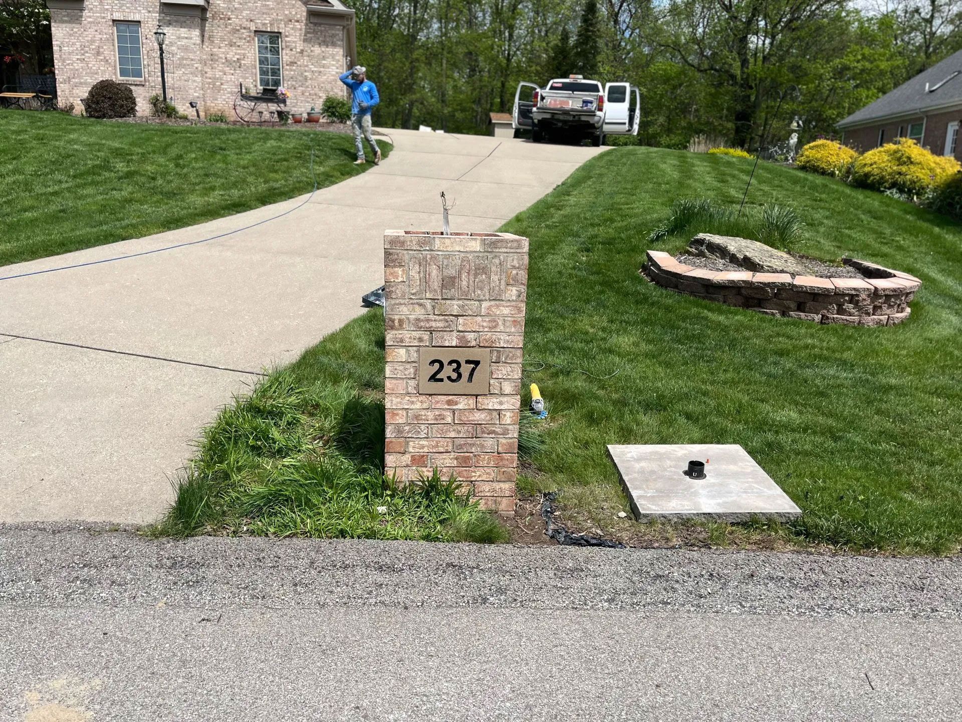 Brick mailbox with address 237 on driveway leading to brick house, vehicle and person in background.