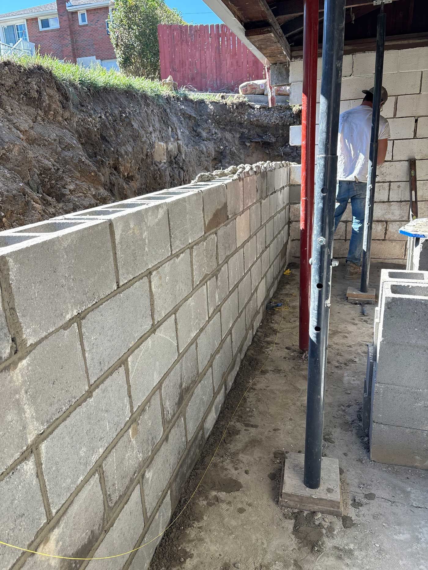 Construction site: cinder block wall being built, worker on ladder, support beams.