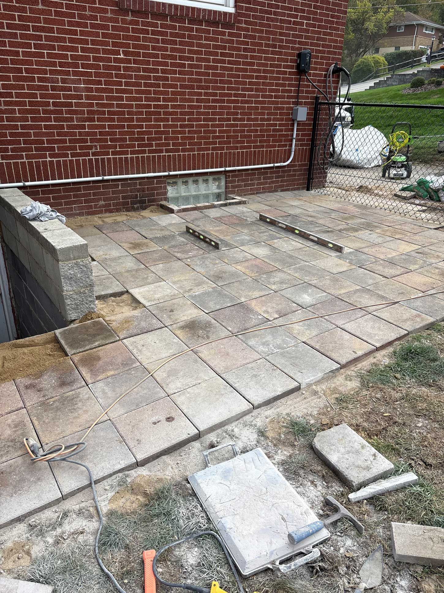 Patio construction: paving stones being laid on a sandy base near a brick building.