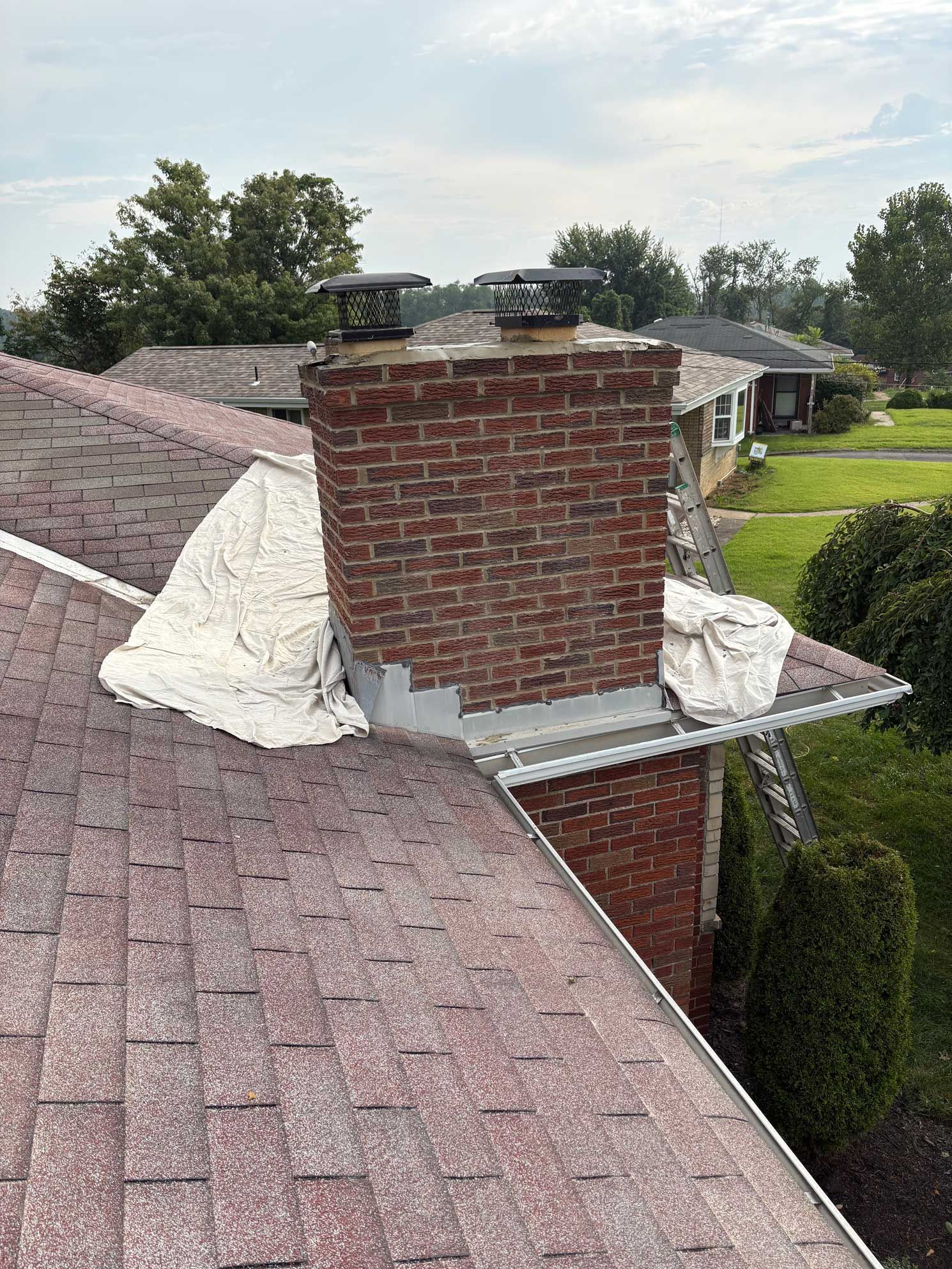 Brick chimney on a shingled roof, tarp covers the roof near the chimney.