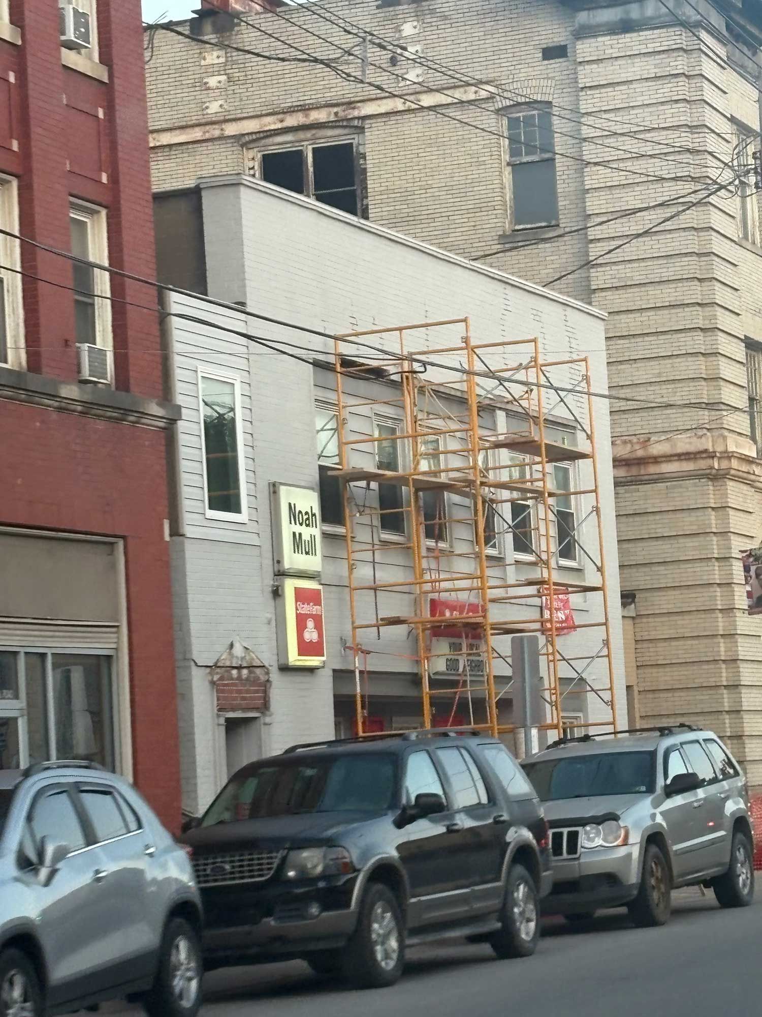 Buildings under construction with scaffolding, cars parked on the street.