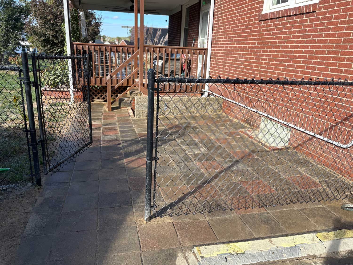 Black chain-link fence surrounds a brick ramp leading to a porch with wooden steps.