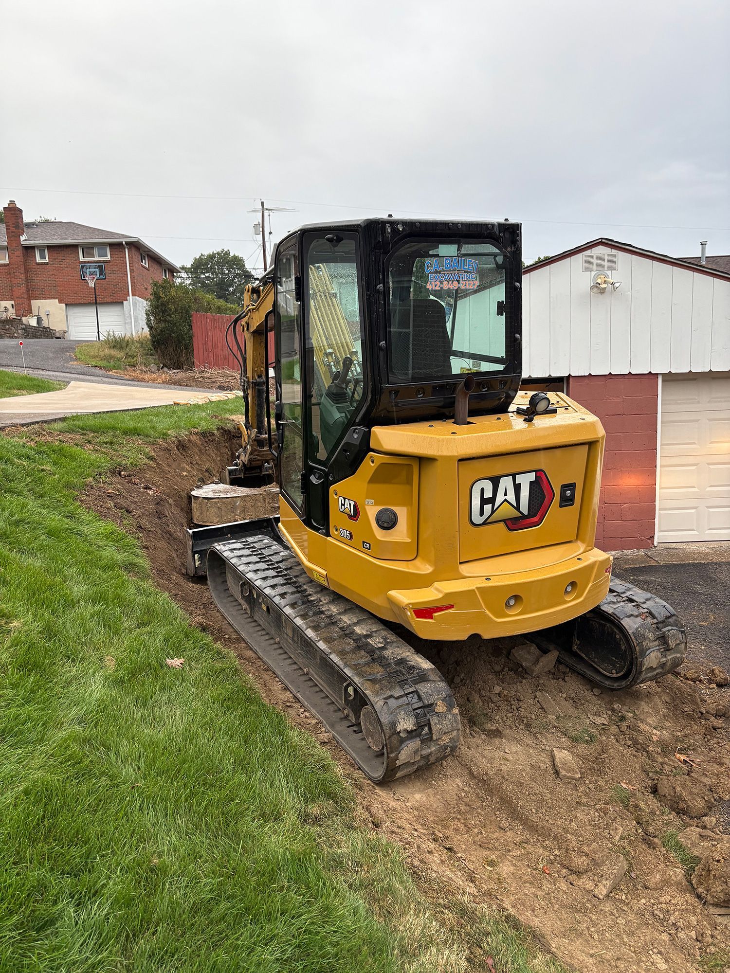 Yellow Caterpillar mini excavator on a grassy slope next to a dirt trench.