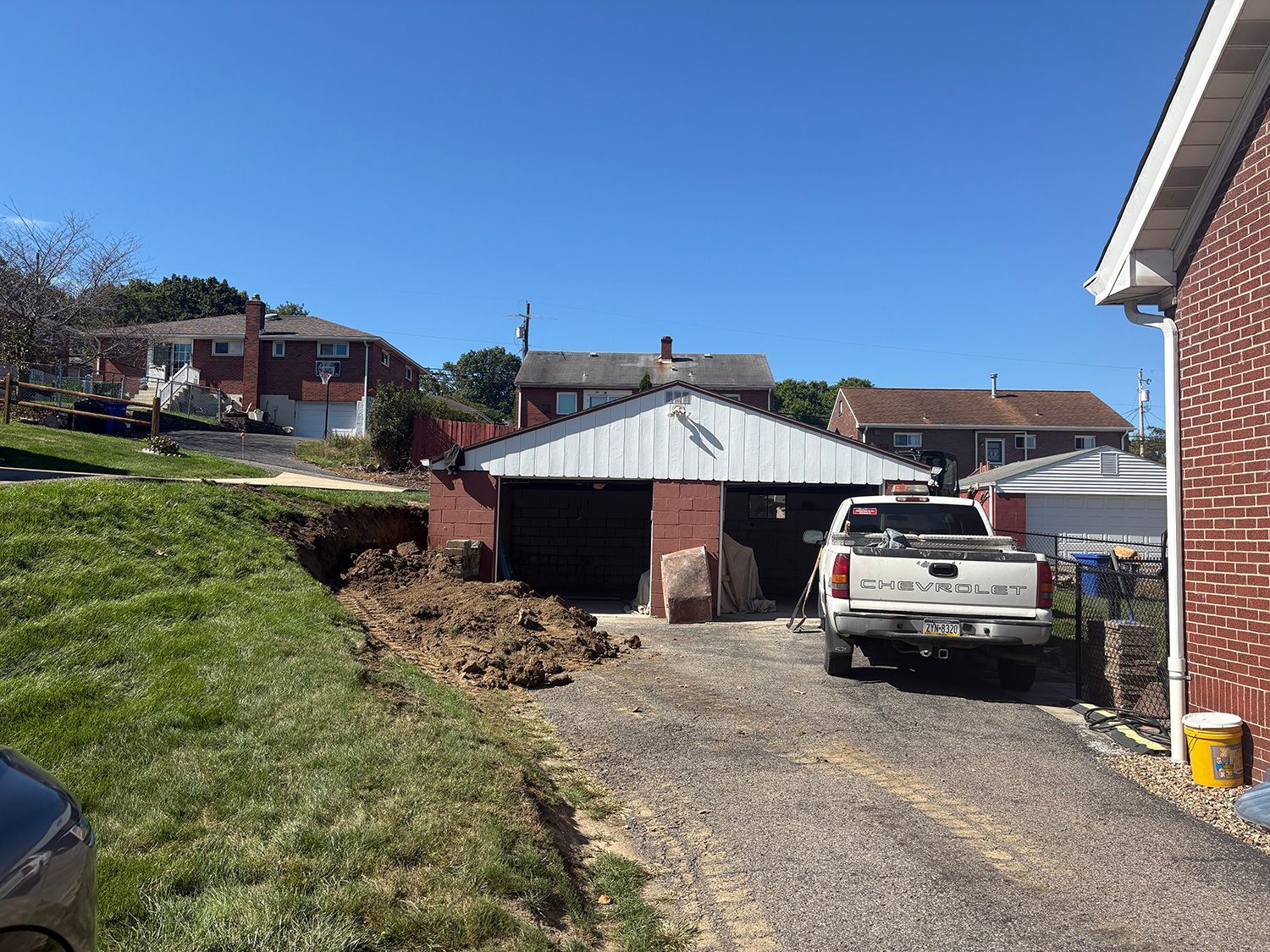 Brick garage with white roof, truck in front, and dirt pile on a sunny day.