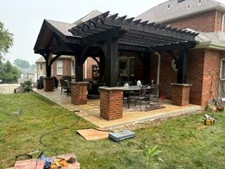 Brick patio with black pergola and outdoor dining set beside a house, with lawn in the foreground