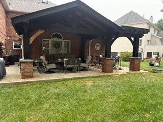 Brick backyard patio with a covered pavilion, outdoor furniture, and a grassy lawn.