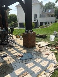 Patio renovation with brick pillar, scattered tools, and stacked pavers in a backyard yard