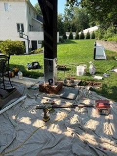 Backyard patio setup with a black pole, tarp, tools, buckets, and a lawn beside an apartment building