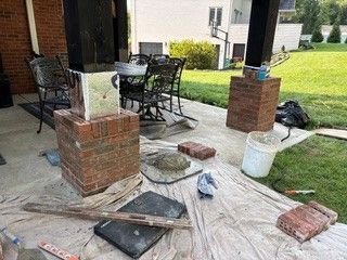 Porch under repair with brick columns, scattered tools, tarp, and debris on the ground