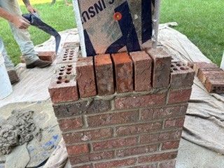 Brick pillar under construction with a worker placing bricks and a bag of cement on top