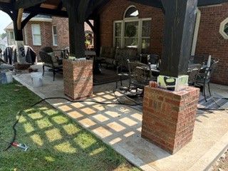 Brick patio with covered seating, metal chairs, and sunlit lattice shadows beside a brick building.