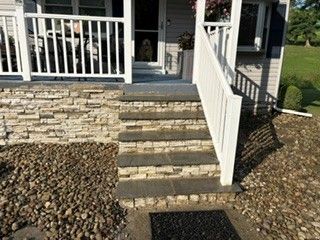 Front porch with stone steps, white railing, and landscaped rock beds by the entrance