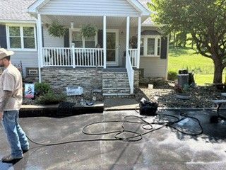 Worker standing by a fire-damaged house with a hose and debris on the driveway