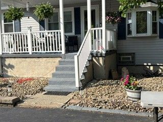Front steps leading to a white porch of a gray house, with stone landscaping and potted flowers.