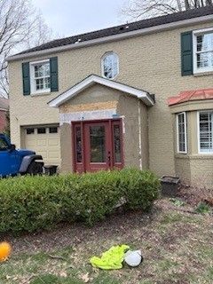 A tan two-story house with a red door and a small area of unfinished, exposed stucco above the front entryway.