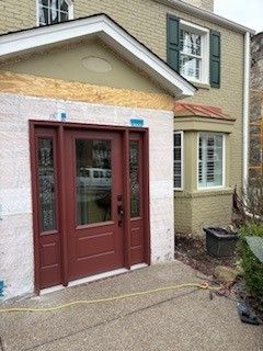 A house with a red front door, unfinished siding, and white trim during a renovation.