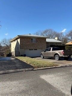 A two-story tan brick house with a garage and a light-colored pickup truck parked in the driveway on a sunny day.
