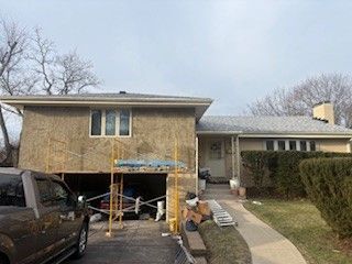 A house with a beige exterior undergoing renovations, featuring a partially open garage and scaffolding on the front.