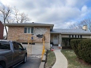 A single-story tan brick house with a dark gray roof, a driveway with a pickup truck, and a walkway leading to the door.